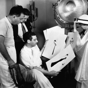THE GAY DIVORCEE, director Mark Sandrich (seated) studying costume sketches on set, 1934