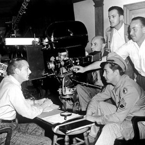 CROSSFIRE, Robert Young, Robert Mitchum, director Edward Dmytryk (tallest head right) filming a scene on set, 1947