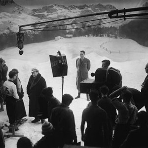THE MAN WHO KNEW TOO MUCH, Leslie Banks (far left, white scarf), Pierre Fresnay (#15), Peter Lorre (dark fur coat, light colored hat), Nova Pilbeam (striped wool cap, bottom), director Alfred Hitchcock (far right), on set, 1934 tmwktm1934y-fsct03(tmwktm193