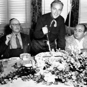 RHYTHM ON THE RANGE, Bing Crosby stands to cut his birthday cake in the company of his father H.L. Crosby (left) and director Norman Taurog (right), 1936