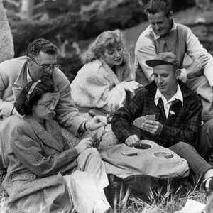 DESIRE ME, director George Cukor, (top left), Greer Garson, (center), play gin rummy with crew on location in Monterey, California, 1947