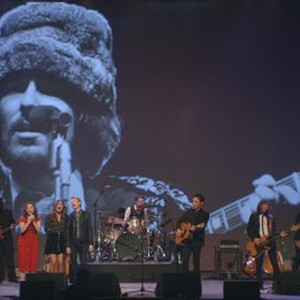 ECHO IN THE CANYON, ON STAGE: FROM LEFT: REGINA SPEKTOR (IN RED DRESS), JADE CASTRINOS, BECK, JAKOB DYLAN (FOREGROUND), CAT POWER (FAR RIGHT) SINGING 'MONDAY, MONDAY'; PHOTOGRAPH ON SCREEN: JOHN PHILLIPS OF THE MAMAS AND THE PAPAS, 2018. © GREENWICH ENTERTAINMENT