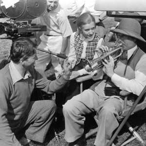 VARSITY SHOW, Johnnie 'Scat' Davis (left) instructing director William Keighley (right) about trumpet playing while chief cameraman Sol Polito (back left) and Priscilla Lane watch, between scenes, 1937