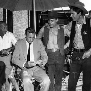 THE HANGMAN, Director Michael Curtiz watches as Gary Cooper rolls his own cigarette while visiting Jack Lord and Fess Parker on set, 1959