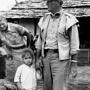 HATARI!, hardy Kruger looks on as John Wayne makes friends with a little girl on set, 1962